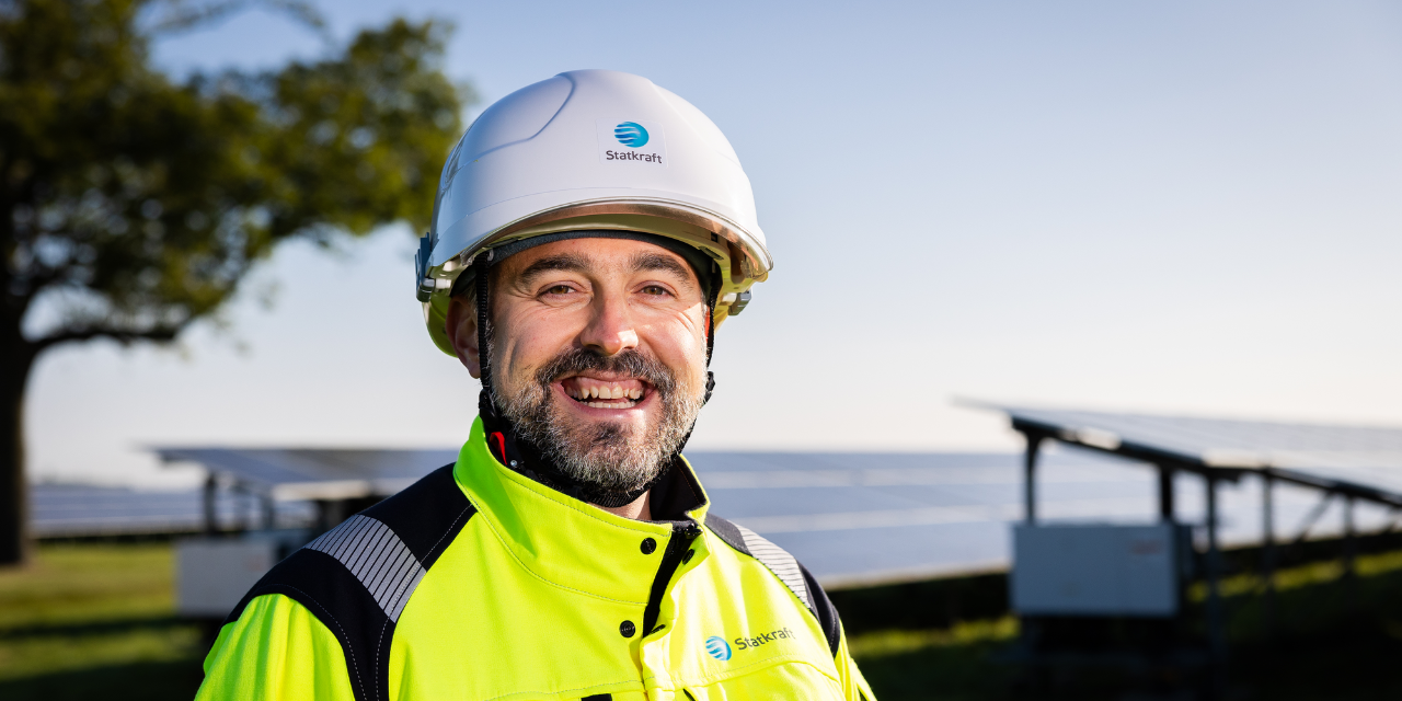 Man wearing safety gear smiling into the camera with solar panels in the background